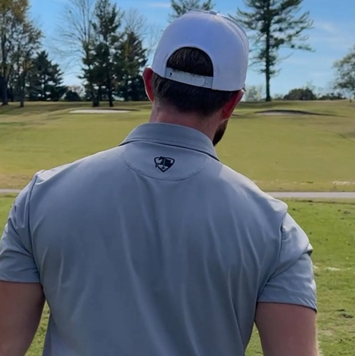 Man in a gray polo shirt and white cap on a golf course