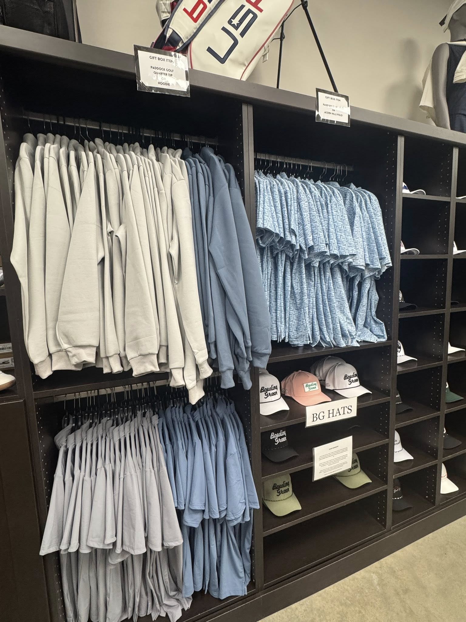 Display of clothing and hats in a store with racks and shelves.